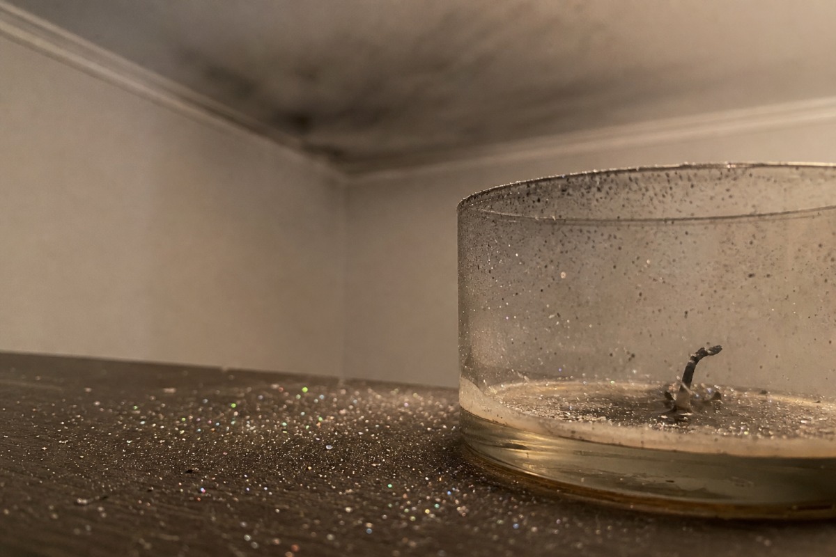 Drobny brokat rozsypany po stole wokół wypalonej świecy, w tle cienki szary nalot sadzy na suficie.
